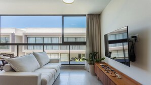 Un salón moderno con un sofá, un televisor de pantalla plana y un balcón con vistas a otros edificios.