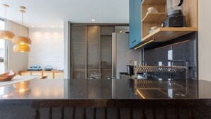 Una cocina moderna con encimera negra, electrodomésticos de acero inoxidable y un estante de madera con adornos.