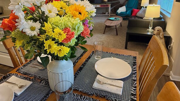 Ett matbord dukat med en vas med blommor, ett glas och bestick.