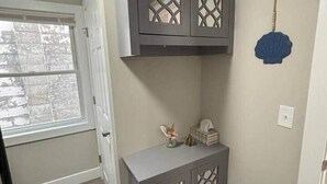 A room with a grey cabinet with decorative cutouts, a small table with a vase and a tissue box, and a blue shell decoration on the wall. - Coastal Comforts - Fire pit (Millcreek Township)