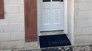A white door with a black doormat that reads "hello," a number "3" on a wooden board, and a small light fixture above the door. - Coastal Comforts - Fire pit (Millcreek Township)