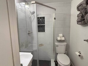 Une salle de bain moderne dotée d’une douche à parois de verre, de toilettes et d’un lavabo.