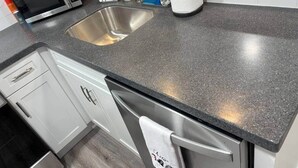 A kitchen with a granite countertop, stainless steel sink, and a microwave. - Coastal Comforts - Fire pit (Millcreek Township)