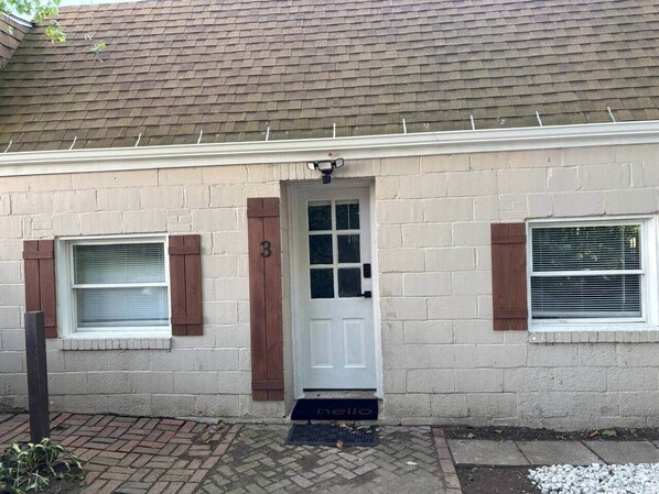 Une maison de plain-pied avec une porte blanche, deux fenêtres dotées de volets et un petit porche.