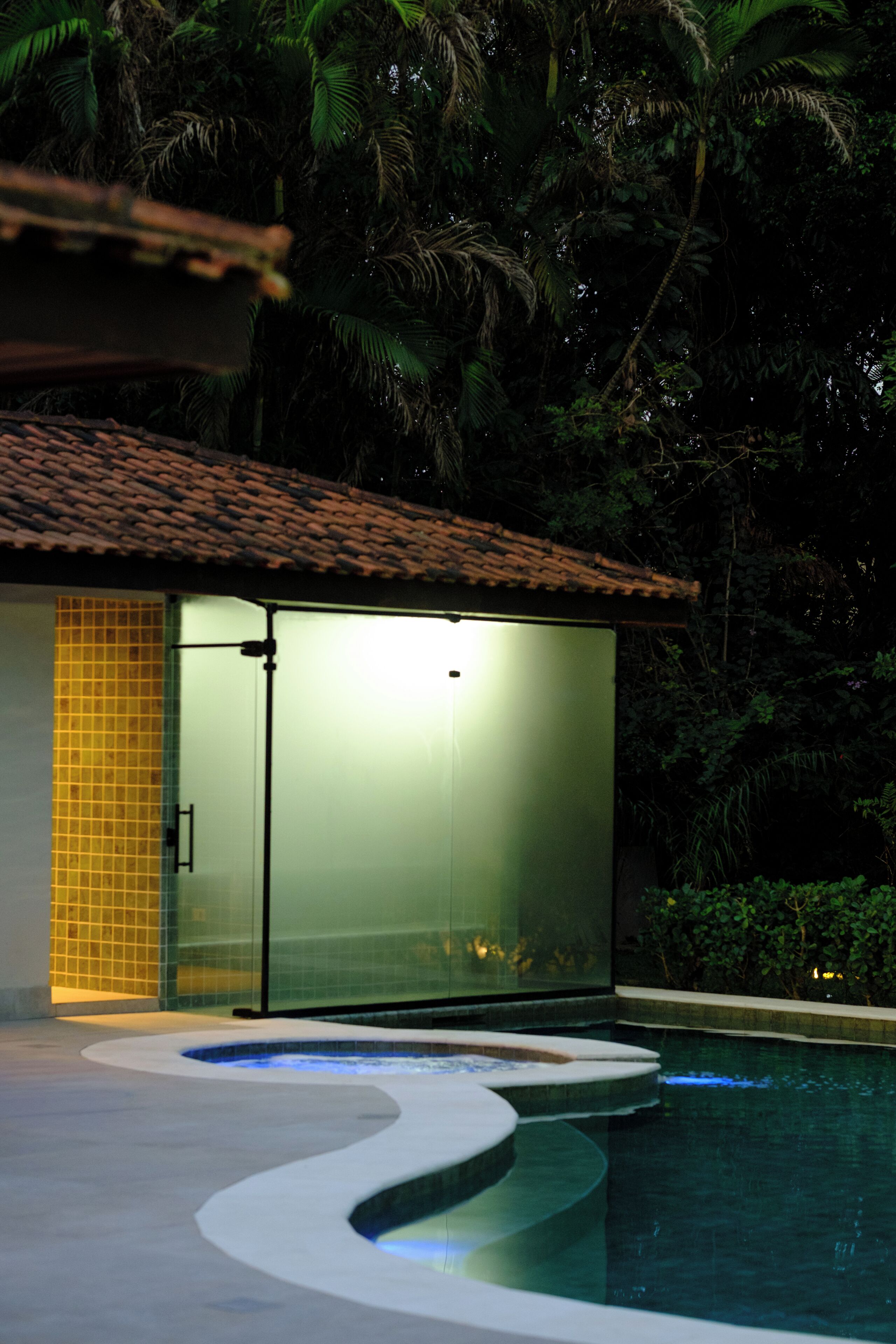 Una piscina con solárium de baldosas y una estructura de cristal con techo de cerámica.