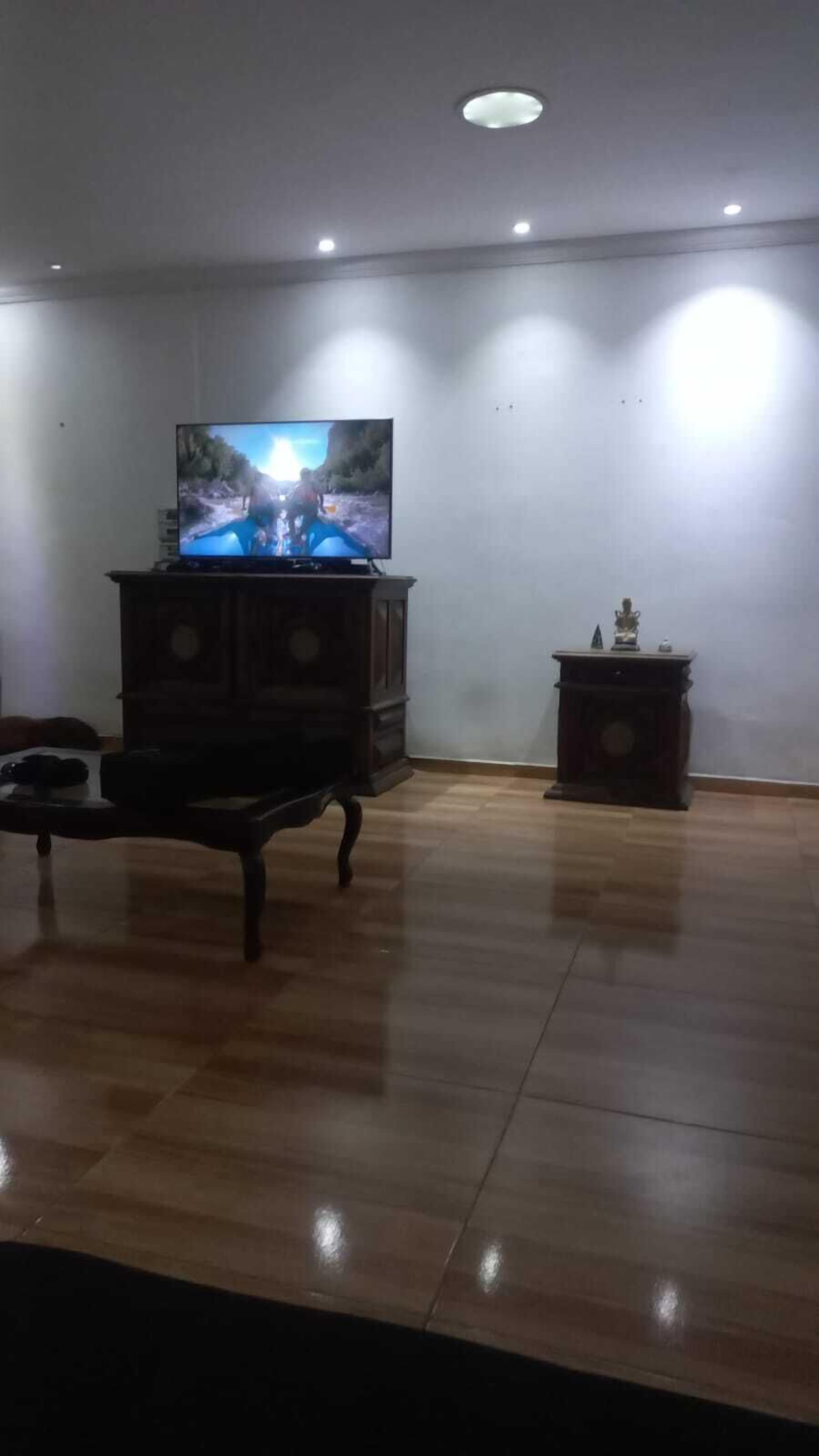 Un salon avec un plancher en bois, un téléviseur posé sur un meuble en bois et une petite table avec une chaise.