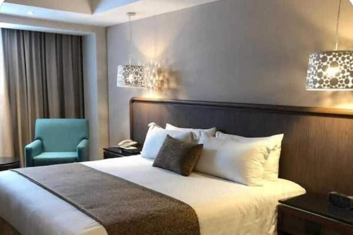 A hotel room with a large bed, a nightstand, a chair, and a lamp.