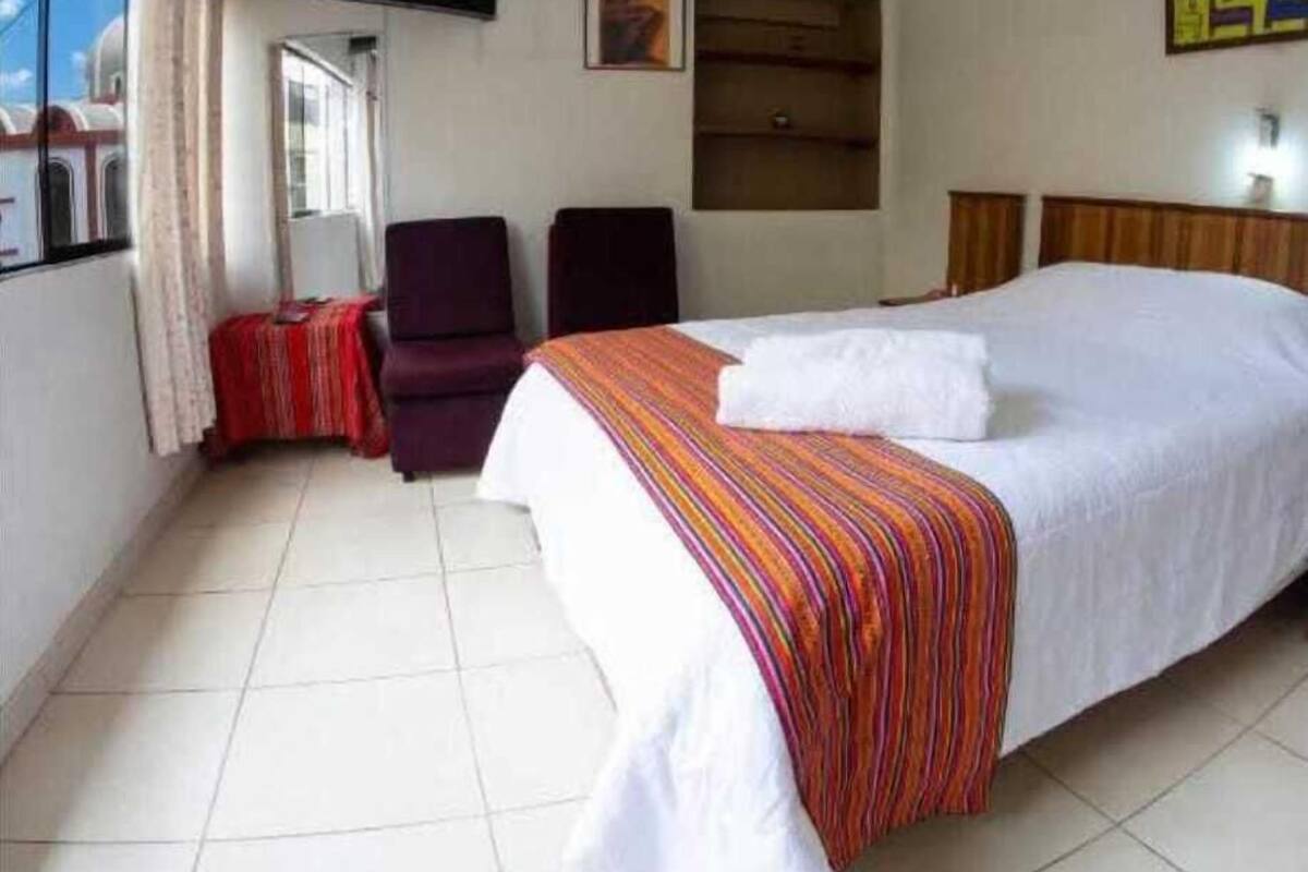 A hotel room with a bed, a chair, a TV, and a window with curtains.