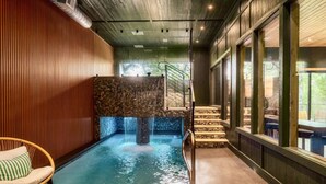 A spa area with a stone wall, a small pool, a wooden chair, and a staircase leading to an outdoor area. - Pool w/ a grotto!/Hot Tub/Game Room/Rooftop Deck - Appalachian Falls (Sevierville)