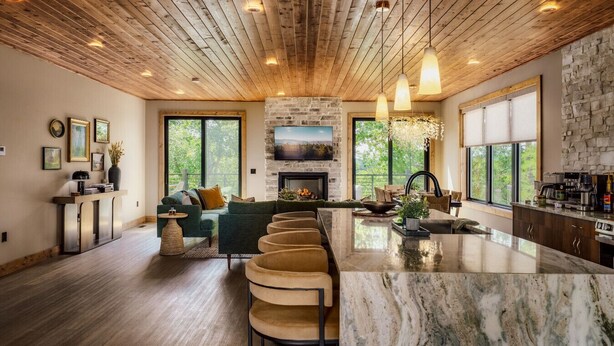A modern kitchen with a stone fireplace, wooden ceiling, and large windows. - Pool w/ a grotto!/Hot Tub/Game Room/Rooftop Deck - Appalachian Falls (Sevierville)