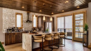 A modern kitchen with a large island, bar stools, and a stone wall. - Pool w/ a grotto!/Hot Tub/Game Room/Rooftop Deck - Appalachian Falls (Sevierville)