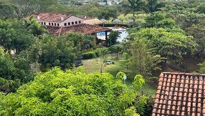 Un hotel con tejado de tejas rojas, rodeado de abundante vegetación y colinas al fondo.