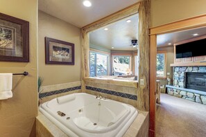 A bathroom with a large bathtub, a wooden-framed mirror, and a stone fireplace in the adjacent living area. - Ski-In/Out, Hot Tub: Spacious Retreat in Whitefish (Whitefish)