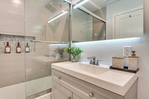 A modern bathroom with a glass shower enclosure, a white vanity with a mirror, and a plant on the countertop. - 4 Mi to SoFi Stadium: Modern Home w/ Fenced Yard (Los Angeles)