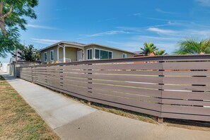 A residential area with a wooden fence, a concrete pathway, and houses with large windows and a covered porch. - 4 Mi to SoFi Stadium: Modern Home w/ Fenced Yard (Los Angeles)