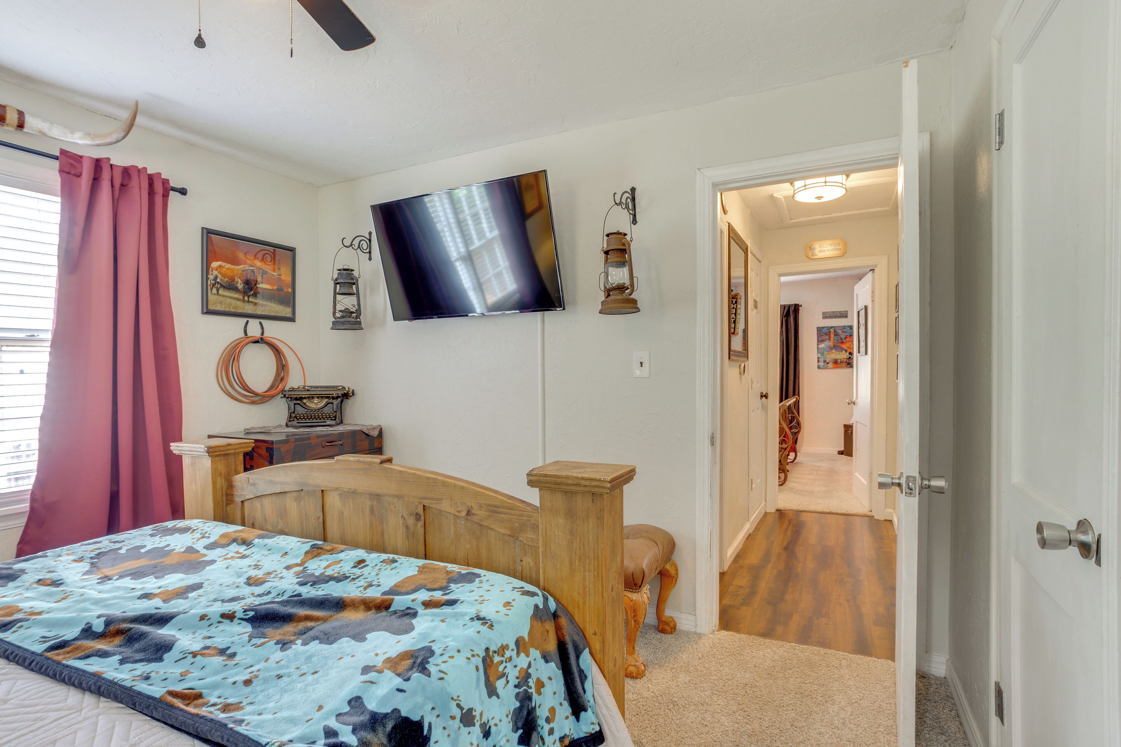 Quarto com cama, televisão, cabeceira de madeira, escrivaninha e porta que dá para outro cômodo.