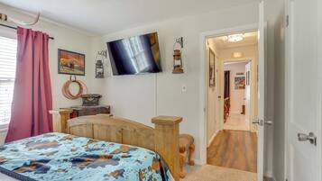 Quarto com cama, televisão, cabeceira de madeira, escrivaninha e porta que dá para outro cômodo.