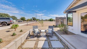 Un patio con dos sillas y una mesa, rodeado por un borde de grava y piedras, y un edificio moderno al fondo.