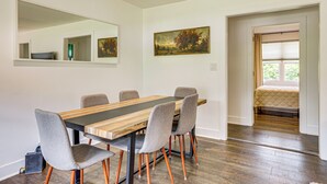 Comedor con una mesa de madera y sillas grises tapizadas, un espejo grande y un cuadro en la pared.