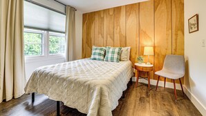Un dormitorio con una cama, una silla, una mesita de noche y una ventana con cortinas.