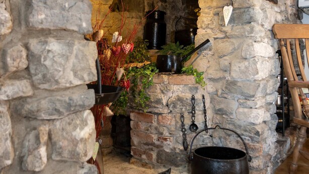 A stone fireplace with a clock, a cat figurine, and various kitchen utensils. - Hall House Estate - 4 Properties- St Florence (Tenby)