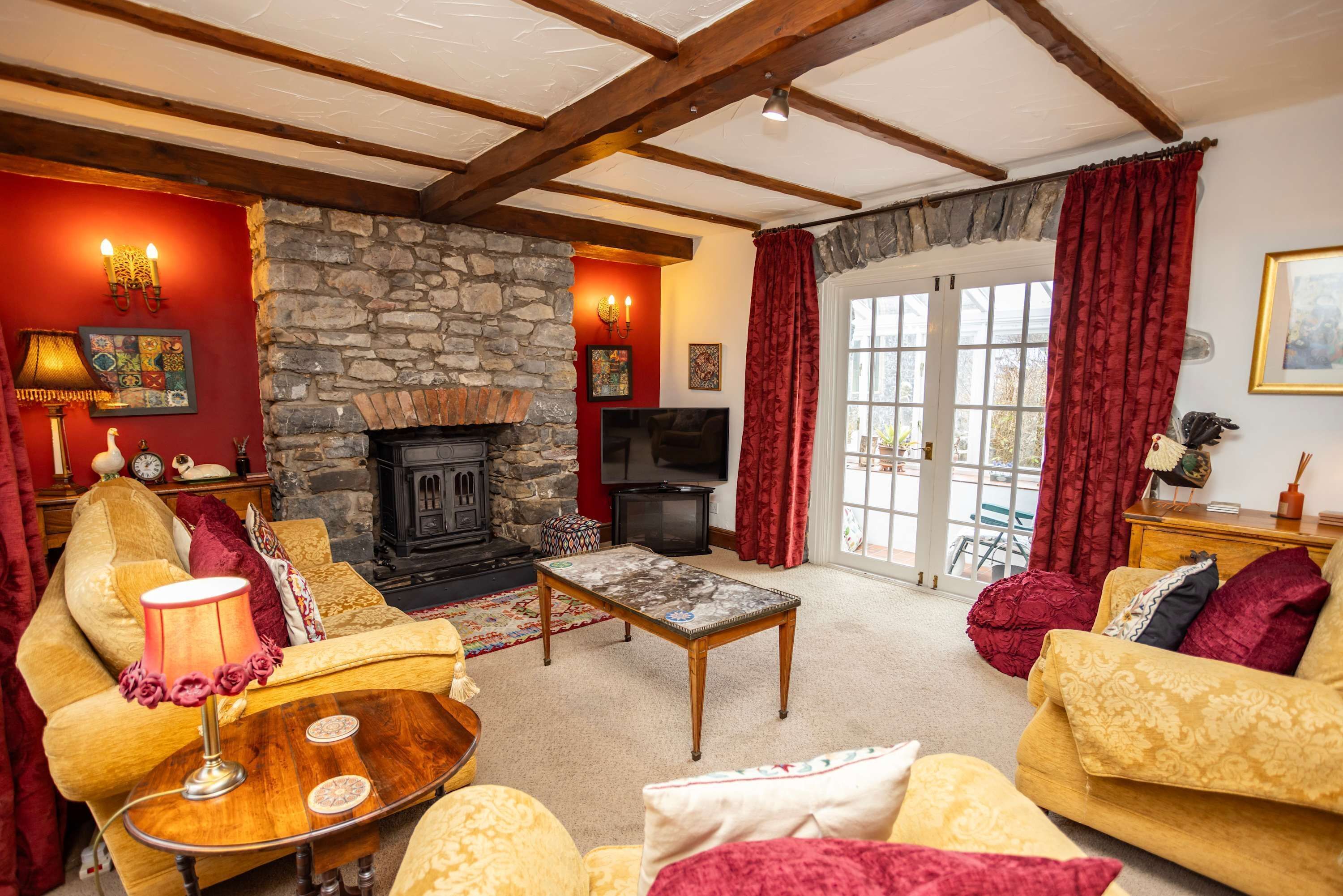 A cozy living room with a stone fireplace, comfortable seating, a television, and a large window with curtains.