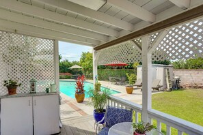 Ein überdachter Patio-Bereich mit Pool, Gartenmöbeln und Kübelpflanzen.