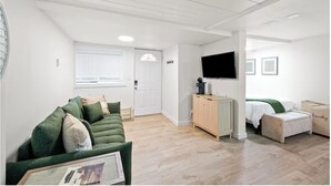 Een ruime woonkamer met een groene bank, een houten kast, een televisie en een bed.