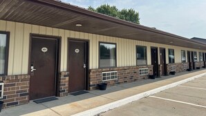 A row of motel rooms with numbered doors, a parking lot, and a clear sky. - Elgin Sleepin Inn (Elgin)
