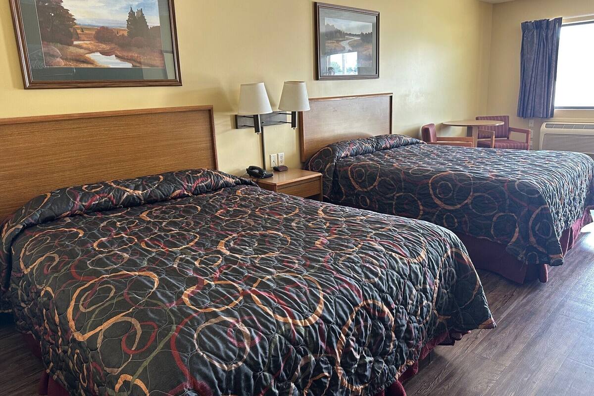 A hotel room with two beds, a nightstand, a lamp, and two framed pictures on the wall.