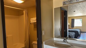 A bathroom with a bathtub, toilet, and sink. There is a mirror above the sink and a window with curtains. - Elgin Sleepin Inn (Elgin)