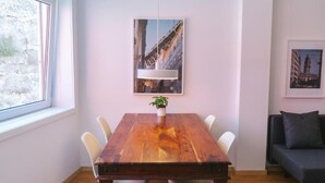 A dining area with a wooden table, white chairs, a hanging pendant light, and a framed picture on the wall. - Porto serenity studio (União de Freguesias do Centro)
