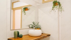 A bathroom with a white marble wall, a wooden vanity, a white sink, and two potted plants. - Porto serenity studio (União de Freguesias do Centro)