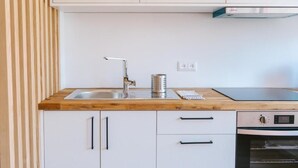 A modern kitchen with white cabinets, a wooden countertop, a stainless steel sink, and a built-in oven. - Porto serenity studio (União de Freguesias do Centro)