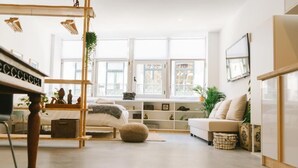 A modern living room with a sofa, a wooden chair, a small table with decorative items, and a large window providing natural light.