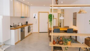 A modern kitchen with white cabinets, a wooden countertop, and a built-in dishwasher. There is a dining area with a wooden table and chairs, and a hanging plant.