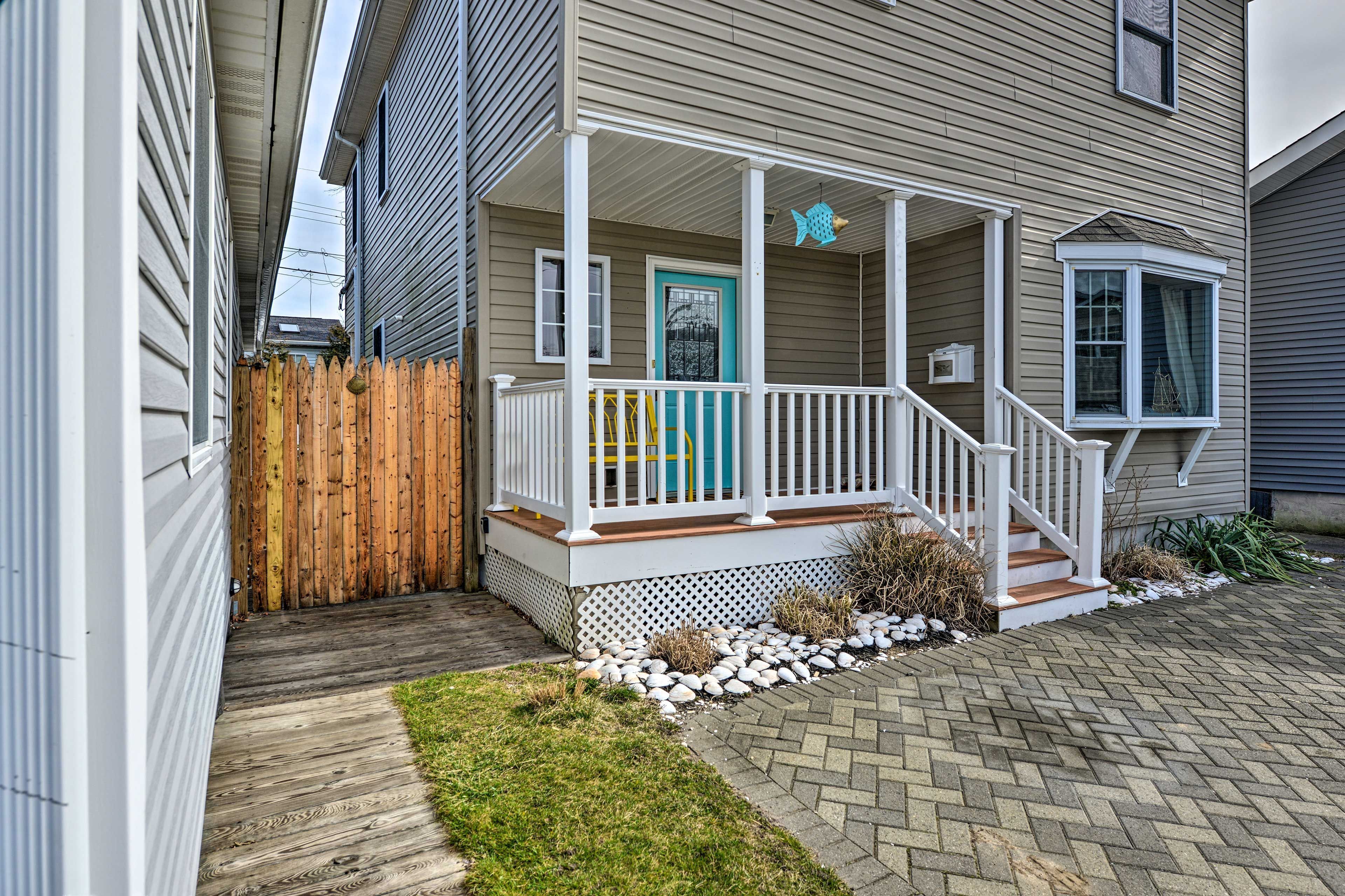 Covered front porch with white railings, a teal door, and a paver driveway.