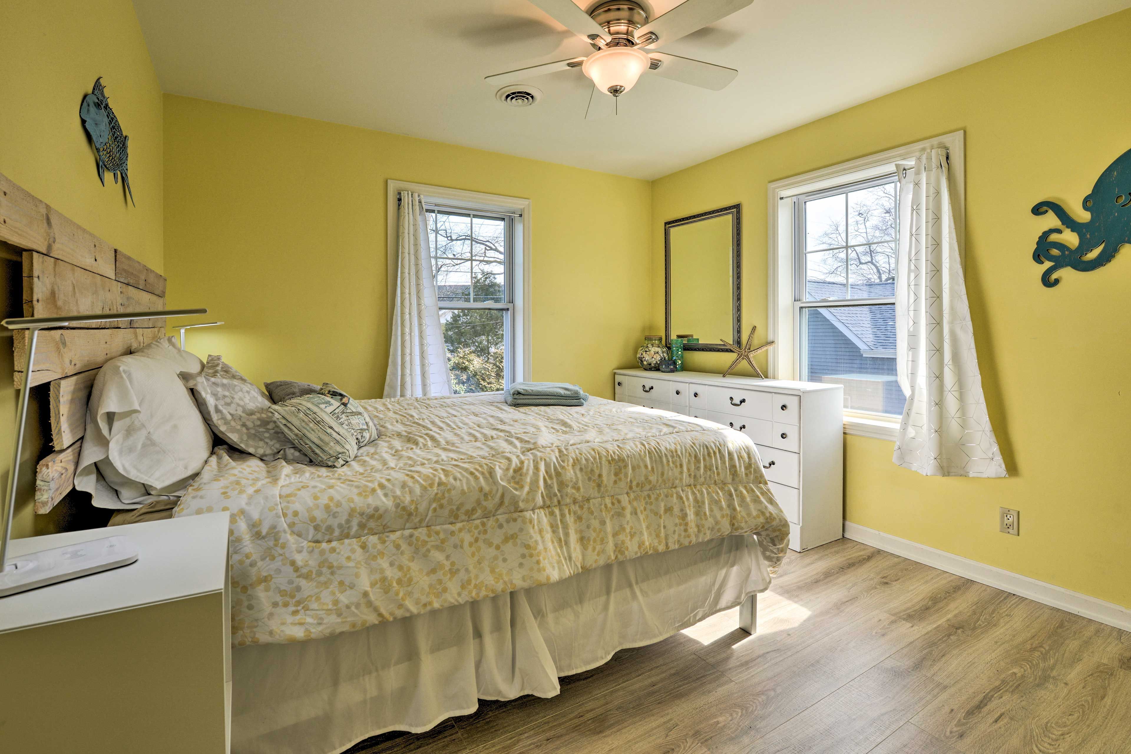 A sunlit bedroom with bright yellow walls, wood-look flooring, and a white dresser.