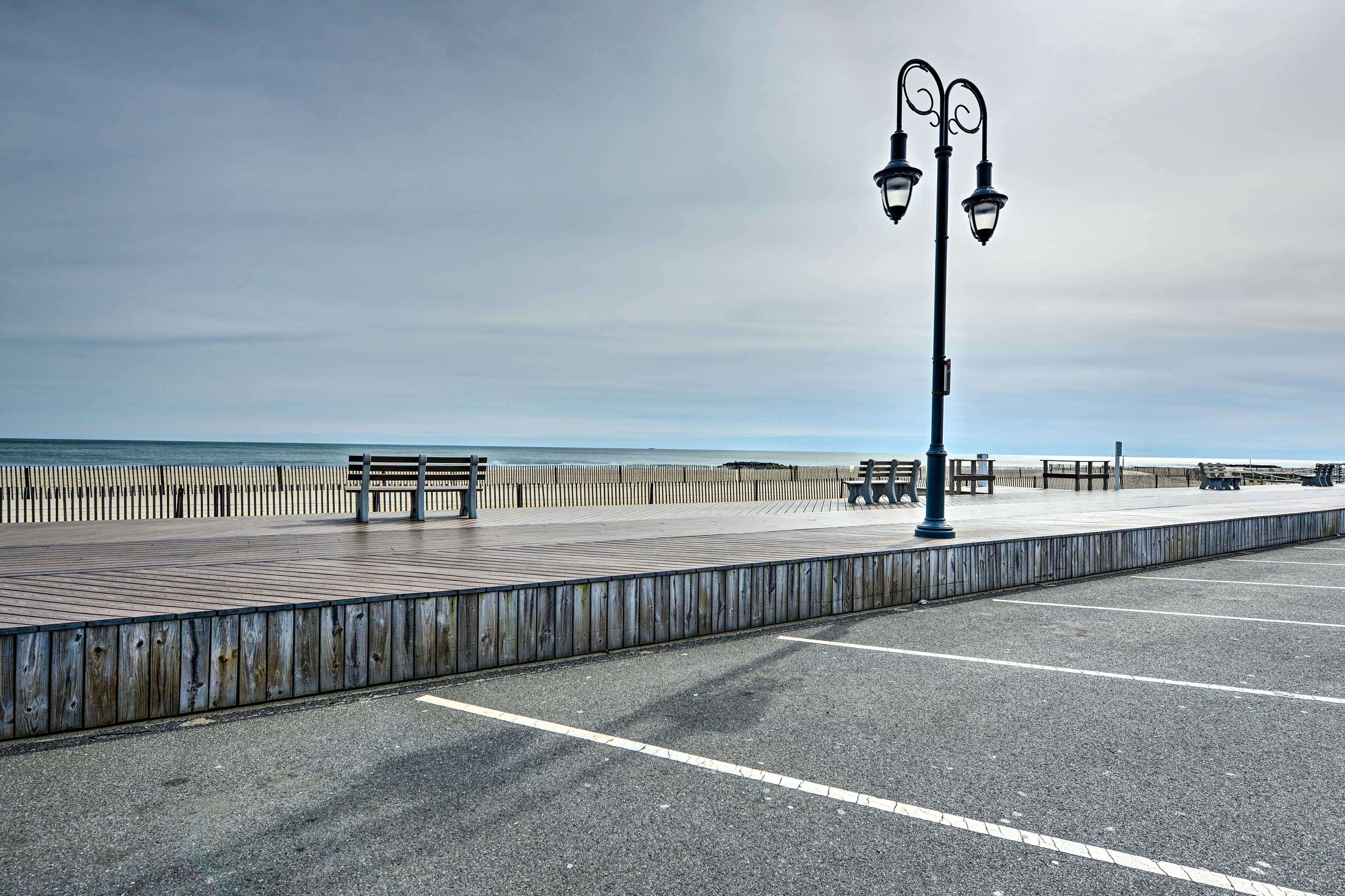 A boardwalk with benches and street lamps, leading to the ocean.