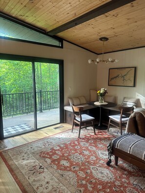 Et værelse med en stor skydedør, der fører ud til en balkon, et rundt spisebord med stole, en sofa og et tæppe.