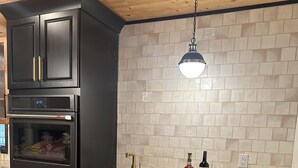 Una cocina con gabinetes negros, un horno de acero inoxidable, una botella de vino y una copa de vino sobre la encimera.