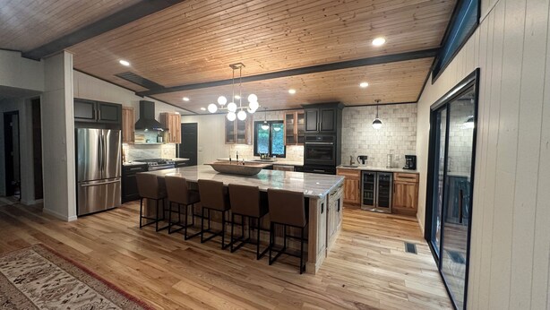 Una cocina moderna con una isla grande, taburetes de bar, electrodomésticos de acero inoxidable y techo de madera.
