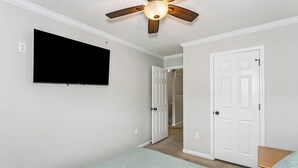 A bedroom with a bed, a ceiling fan, a TV mounted on the wall, and a door leading to another room. - Southeast Crestview near I-10 (Crestview)