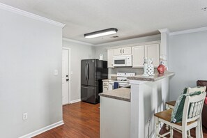 Una cocina compacta con armarios blancos, un refrigerador de acero inoxidable, un microondas y una estufa.