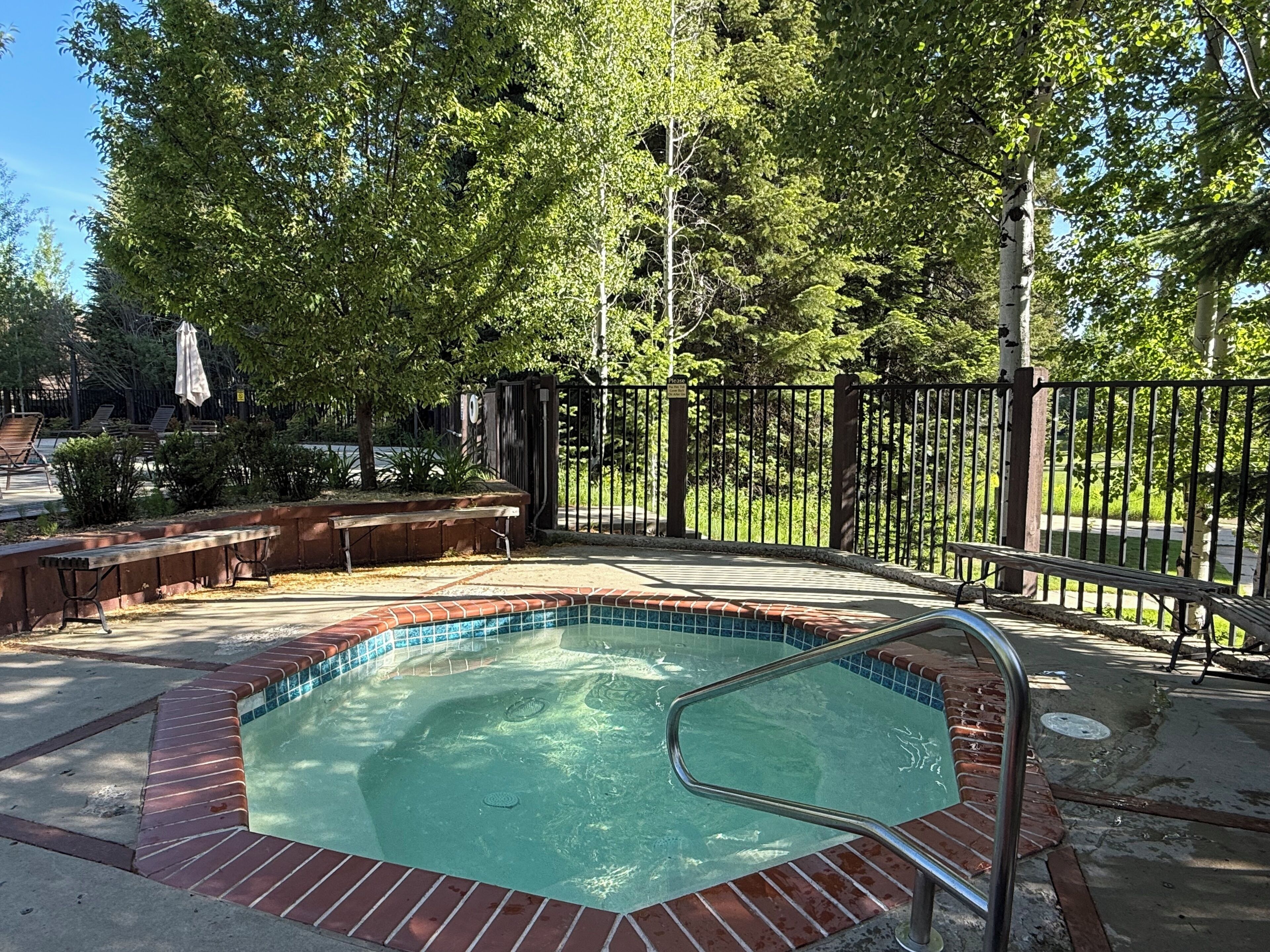 A swimming pool with a brick border, surrounded by a fence and trees.