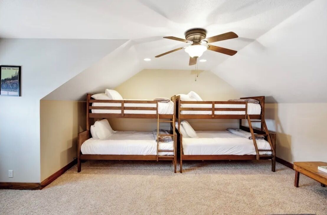 Une chambre de dortoir avec des lits superposés, un ventilateur de plafond et une petite table.