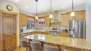 Cocina moderna con encimeras de granito, electrodomésticos de acero inoxidable, armarios de madera y una isla grande con taburetes de bar.