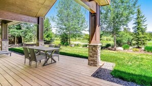 Un patio exterior con terraza de madera, pilares de piedra y una mesa con sillas.