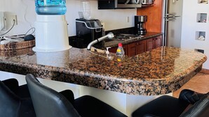 Cozinha com bancadas de granito, armários de madeira, geladeira de aço inoxidável, micro-ondas e cafeteira.