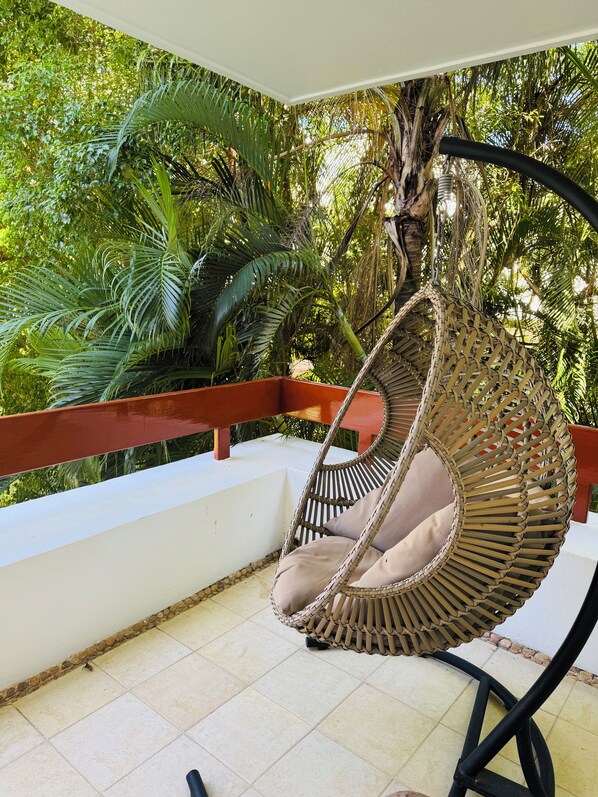 A wicker swing chair with a cushion, positioned on a balcony with a tiled floor and a red railing. - Beach front 1 bedroom condo in beautiful Cozumel. with AC and free WIFI (Q.R.)